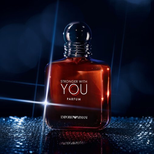 A single bottle of Emporio Armani "Stronger With You Parfum" stands upright on a reflective surface, illuminated by dramatic blue and white lighting against a dark background.