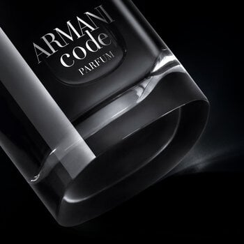 A close-up, angled view of the bottom of an Armani Code Parfum bottle, showcasing its clear glass base and part of the dark body with the silver logo, dramatically lit against a black background.