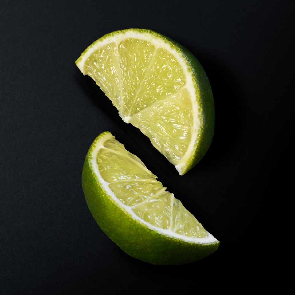 Two vibrant green lime slices, cut and separated, showcasing their juicy pulp on a dark background.