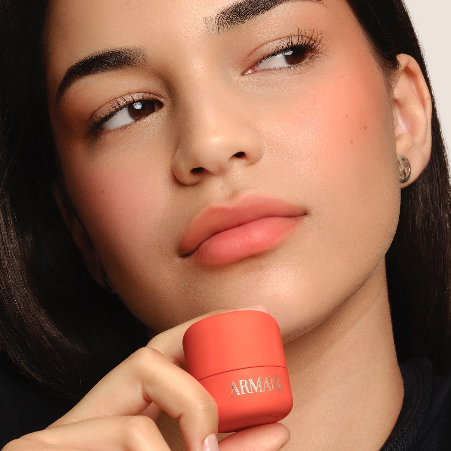Model holding coral Armani Beauty Dolci Blush, a cream-to-powder blush with a natural finish.