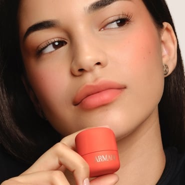Model holding coral Armani Beauty Dolci Blush, a cream-to-powder blush with a natural finish.