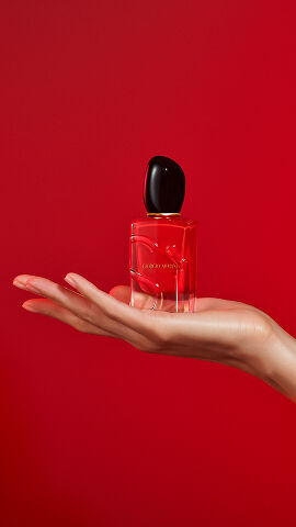 Hand holding the Giorgio Armani Si Passione Eau de Parfum on red background.