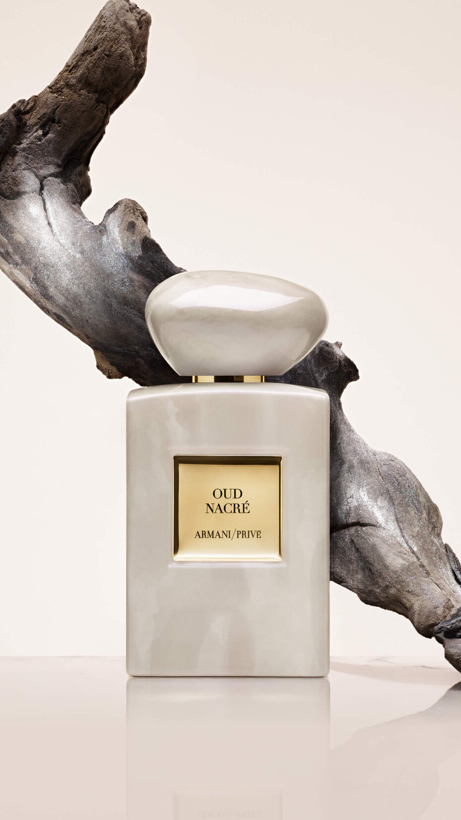 Armani/Prive Oud Nacre: luxurious pearl-toned bottle set against sculptural driftwood, highlighting the fragrance’s rich woody ambery character and elevated artistry.