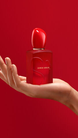 Hand holding the Giorgio Armani Si Eau de Parfum Red Bloom on red background.