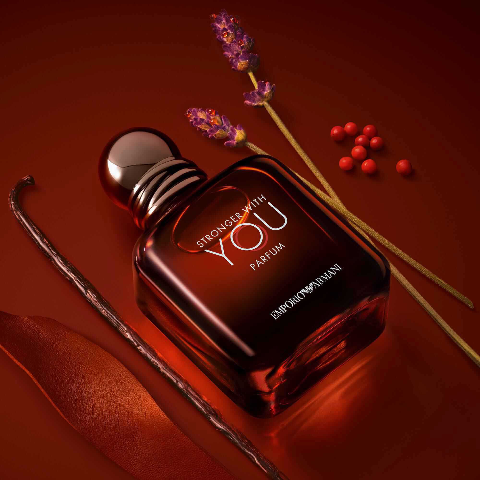 Emporio Armani Stronger With You Parfum — 100ml deep red bottle surrounded by key olfactive ingredients: lavender, pink pepper, vanilla, and leather accord on a rich amber background.