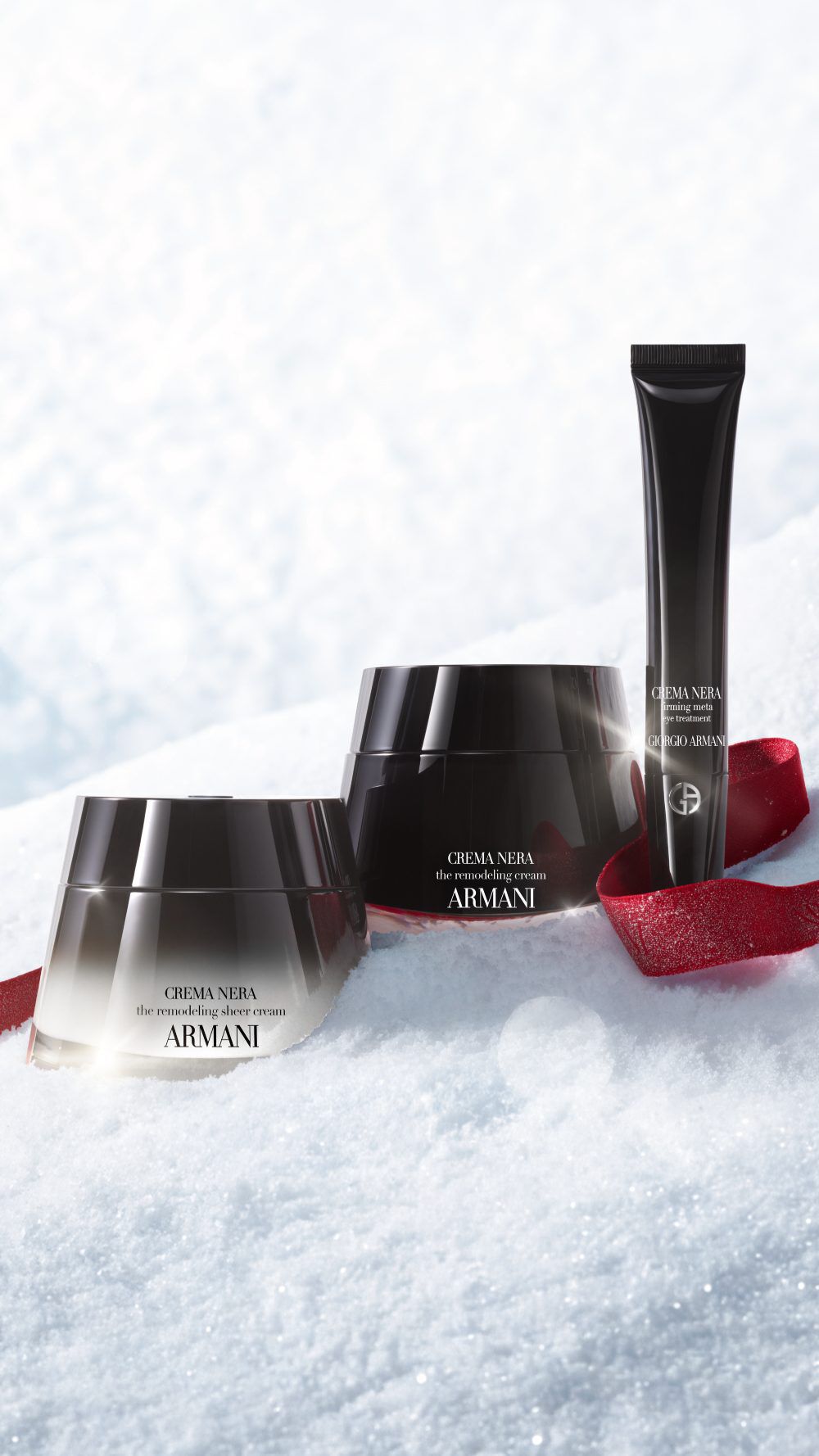 Armani beauty skincare products on snow with a red ribbon for the holiday season.