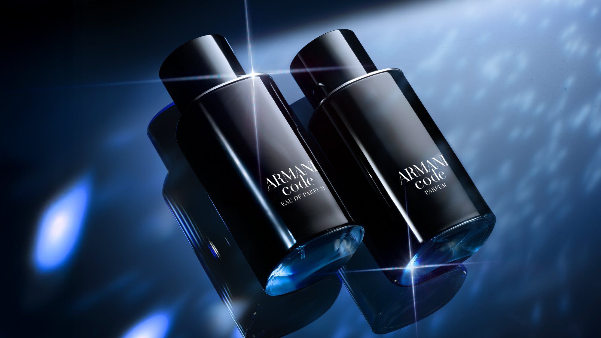 Two sleek black Armani Code bottles are displayed side by side on a reflective blue surface, illuminated by dramatic, sparkling light effects in the background.