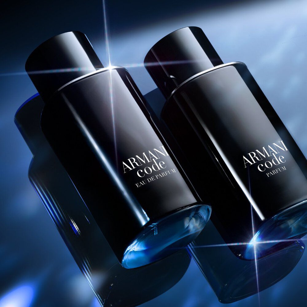 Two sleek black Armani Code bottles are displayed side by side on a reflective blue surface, illuminated by dramatic, sparkling light effects in the background.