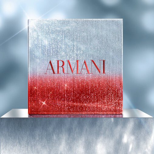 Square Armani holiday gift box in red and silver glitter gradient, displayed on a metallic pedestal with a sparkling, festive blue background.