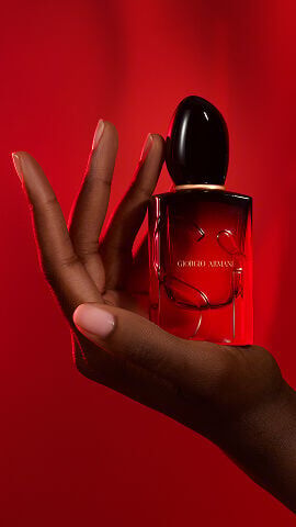 Hand holding the Giorgio Armani Si Passione Eau de Parfum Intense on red background.