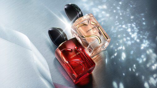 Two Armani Si Passione perfume bottles styled on a blue fabric background with sparkling light effects