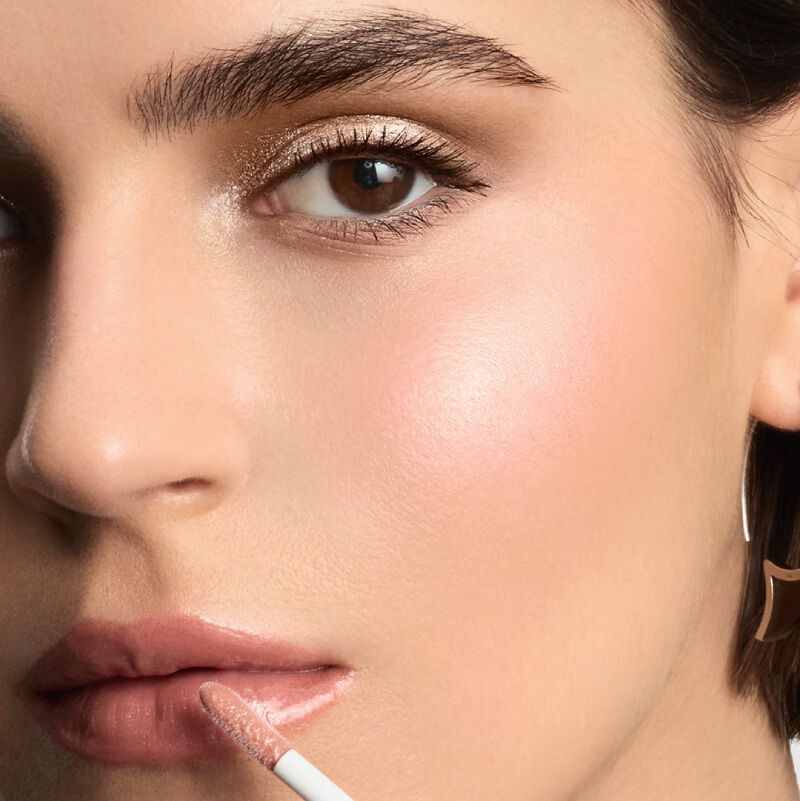 A model applying matte and sparkling lip gloss to their lips with a wand applicator.