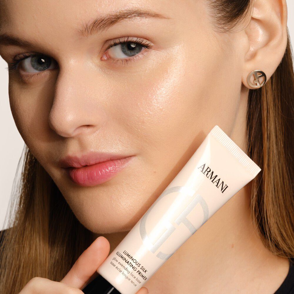 Model with radiant complexion holding Armani Beauty Luminous Silk Illuminating Primer.