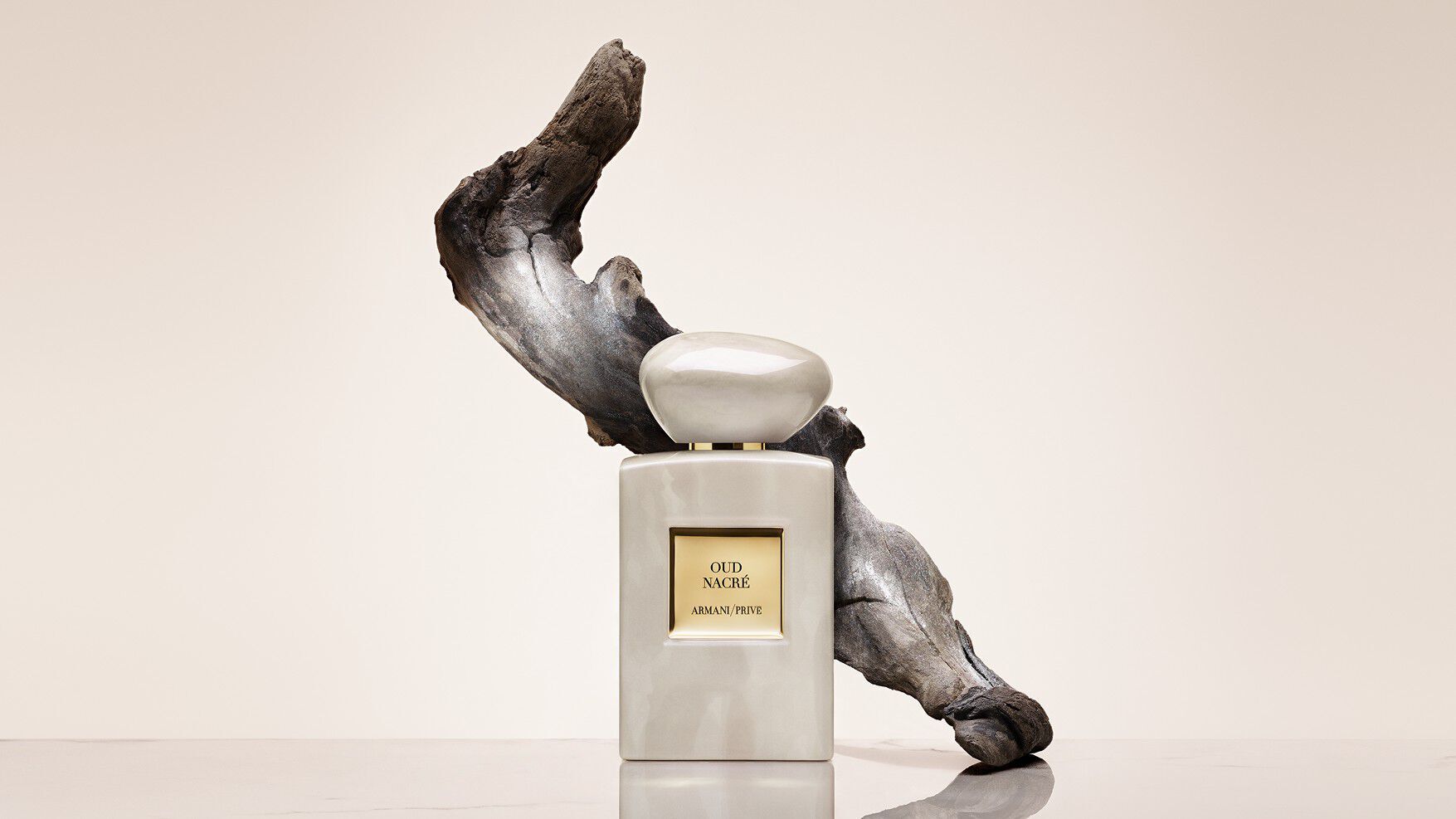 Bottle of Armani/Prive Oud Royal fragrance against a warm background with  an opulent black flower.