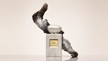 Bottle of Armani/Prive Oud Royal fragrance against a warm background with an opulent black flower.