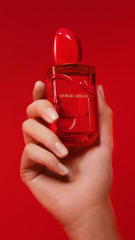 Hand holding the Giorgio Armani Si Eau de Parfum Red Musk on red background.