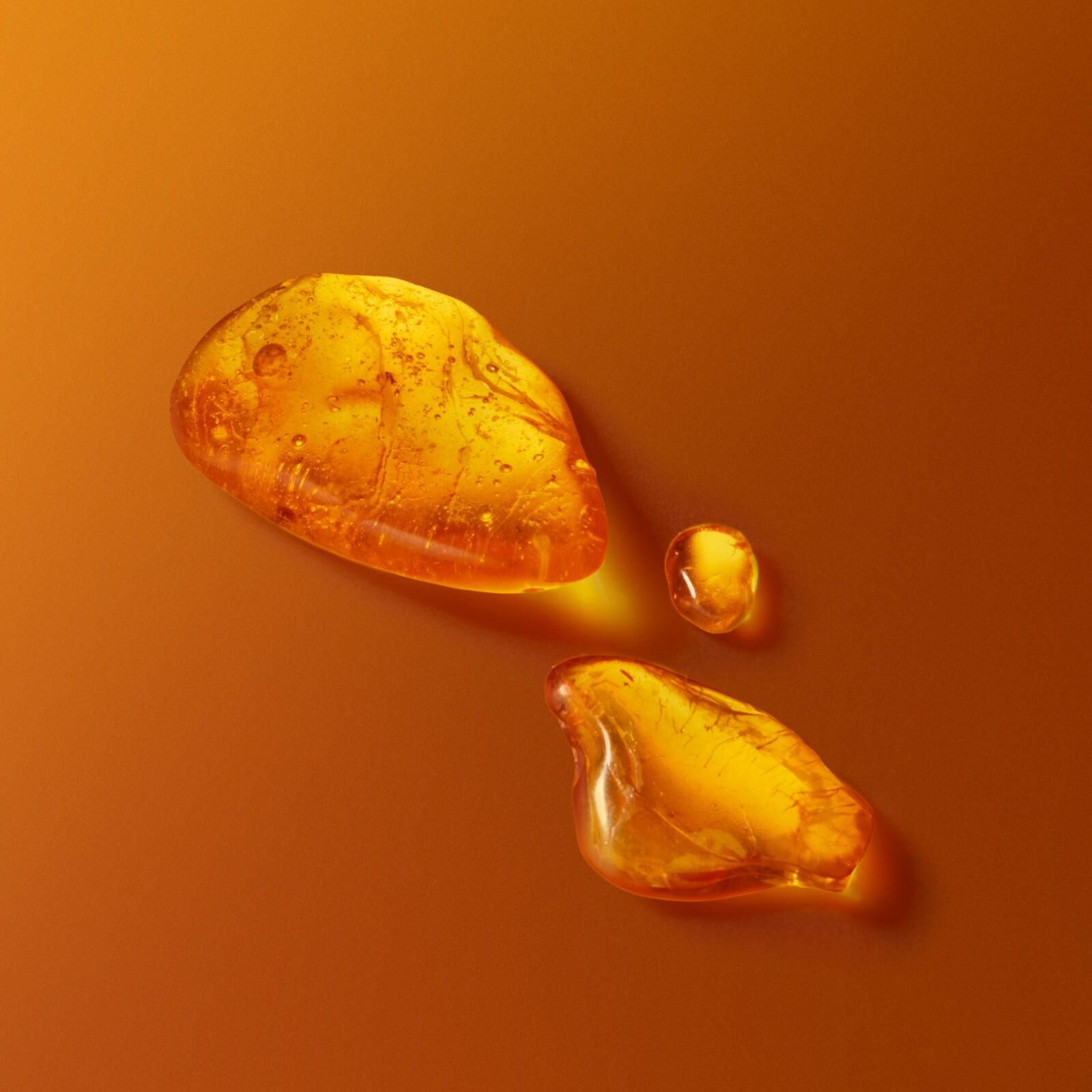 Golden amber droplets and resin pieces on warm orange backdrop representing fragrance essence
