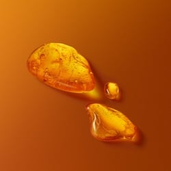 Golden amber droplets and resin pieces on warm orange backdrop representing fragrance essence