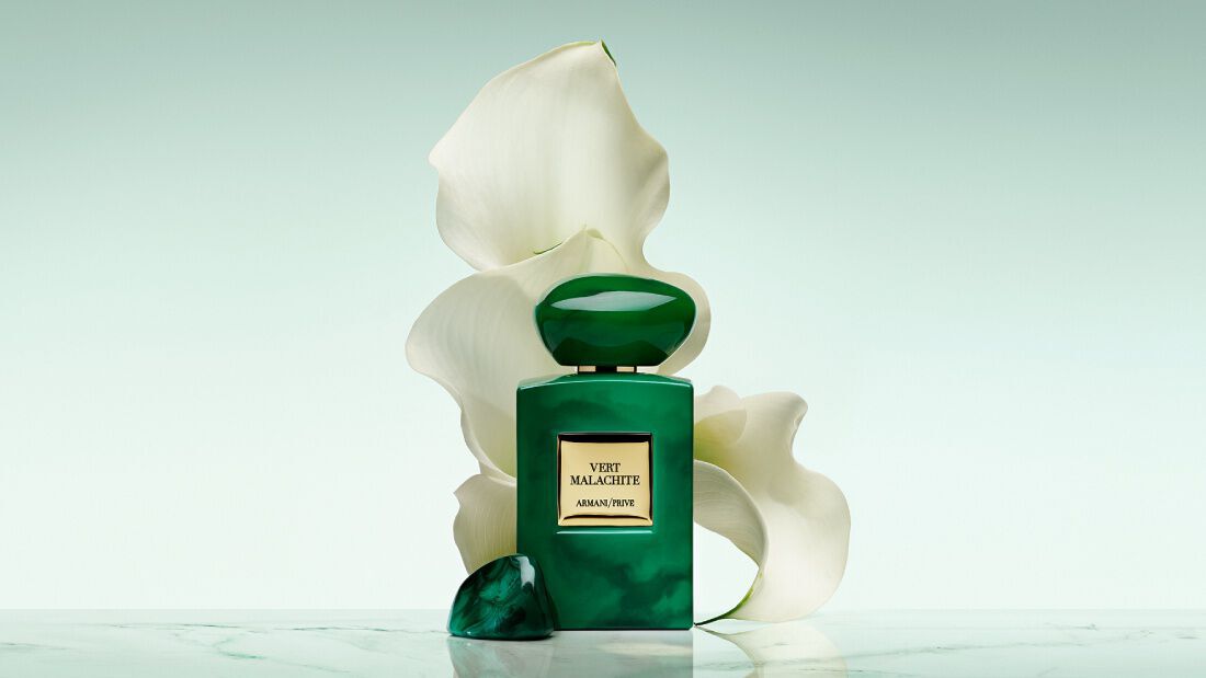 Bottle of Armani/Prive Oud Royal fragrance against a warm background with  an opulent black flower.
