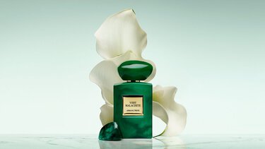 Bottle of Armani/Prive Oud Royal fragrance against a warm background with an opulent black flower.