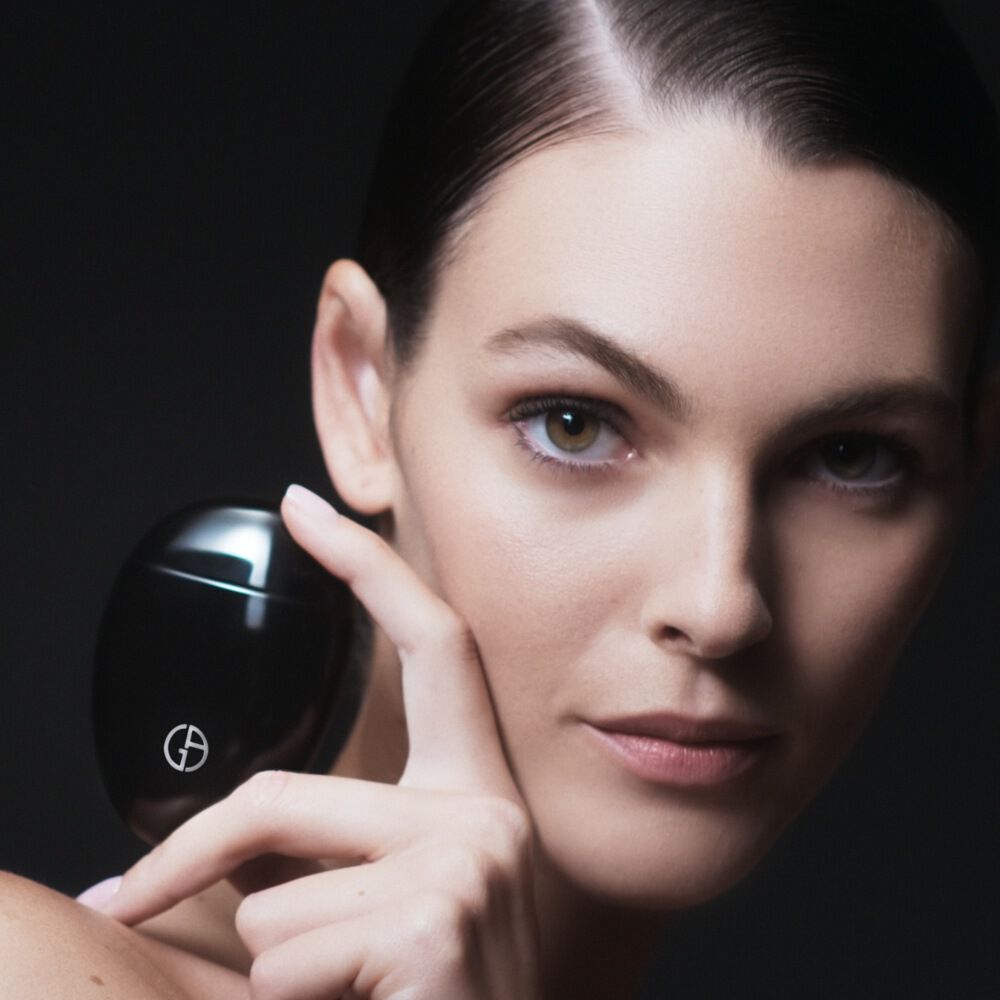 Woman holding Armani beauty THE HAND CREAM beside her face, highlighting the hand and nail treatment.