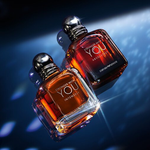 A single bottle of Emporio Armani "Stronger With You Parfum" stands upright on a reflective surface, illuminated by dramatic blue and white lighting against a dark background.