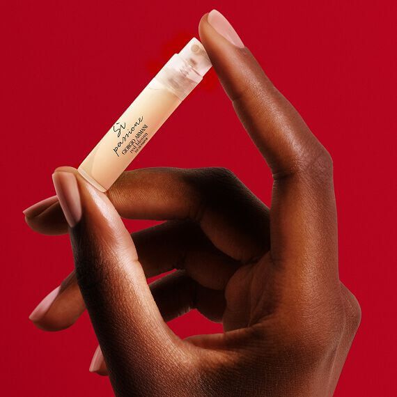 Hand holding a Giorgio Armani Si Passione perfume sample on a red background.