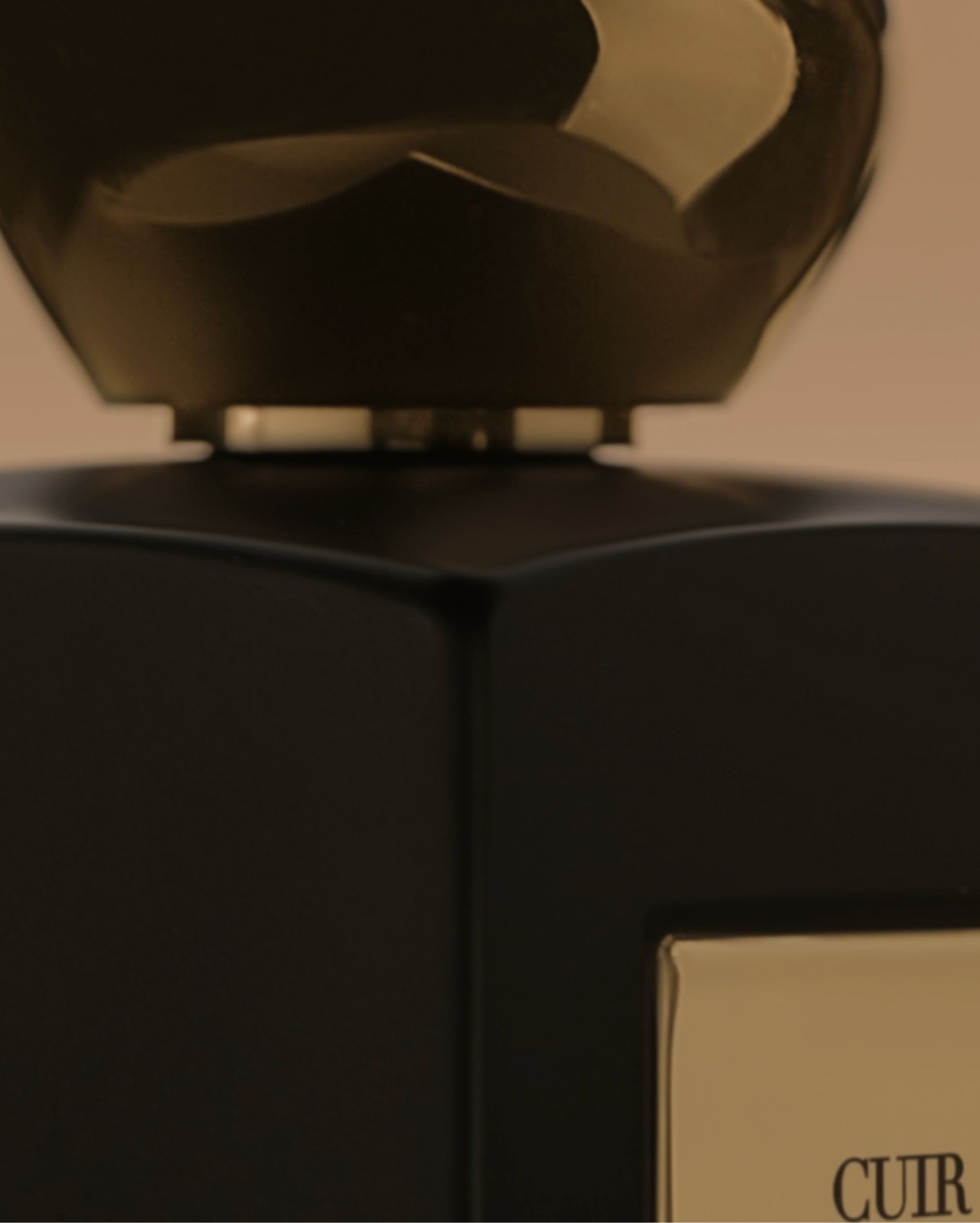 Packshot of Cuir Nu fragrance by Armani/Prive – black bottle with gold plaque and sculptural cap on white background