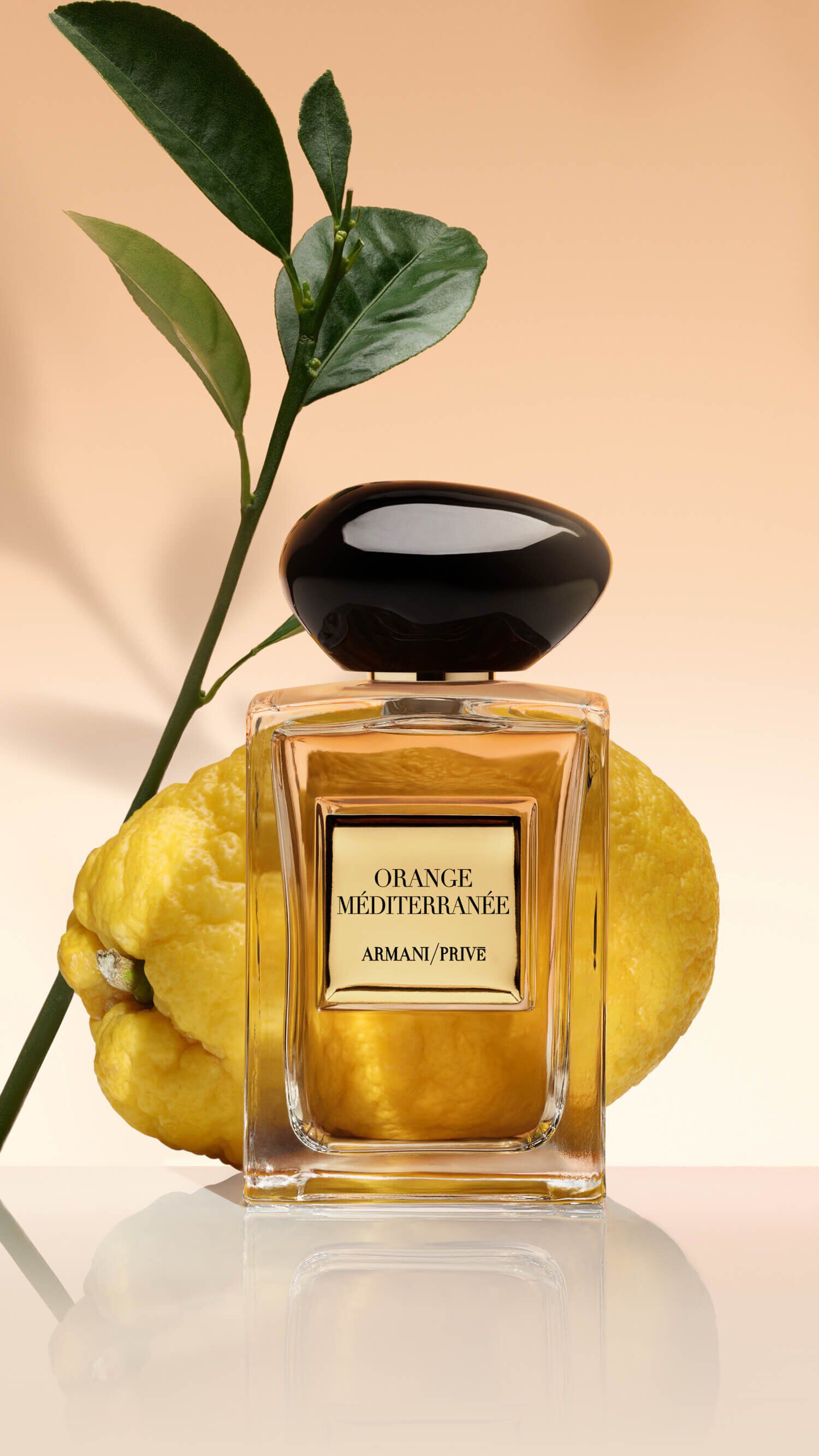 Bottle of Armani/Prive Orange Mediterranee against a light orange background with lemon and citrus ingredients.