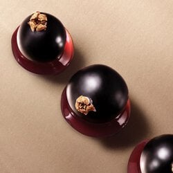 Three glossy blackcurrants with brown tops on a beige background.