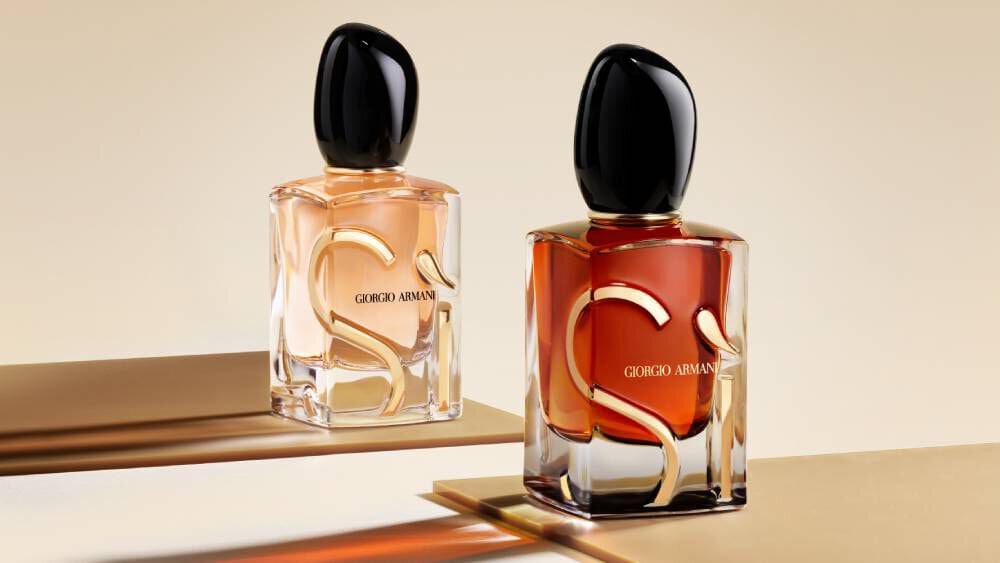 Two Giorgio Armani Si perfume bottles, one lighter and one darker, standing side-by-side on a subtly reflective surface.