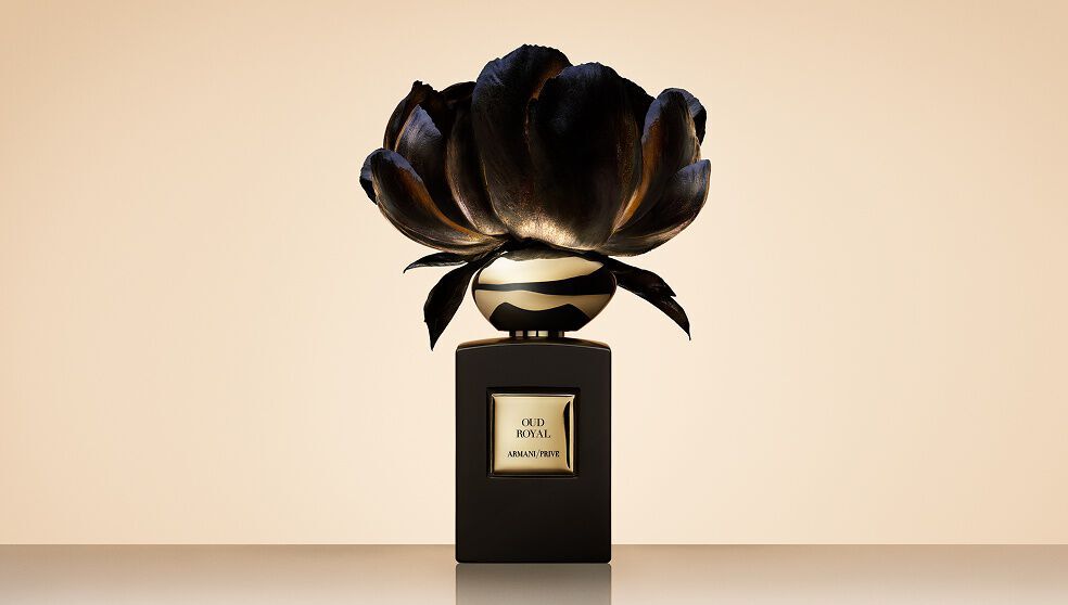 Armani/Prive Oud Royal fragrance bottle against a beige backgound with an opulent black flower.