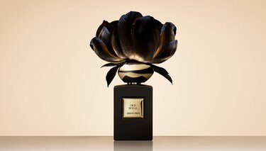 Armani/Prive Oud Royal fragrance bottle against a beige backgound with an opulent black flower.