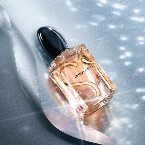 Giorgio Armani Si Eau de Parfum perfume bottles styled on a blue fabric background with sparkling light effects