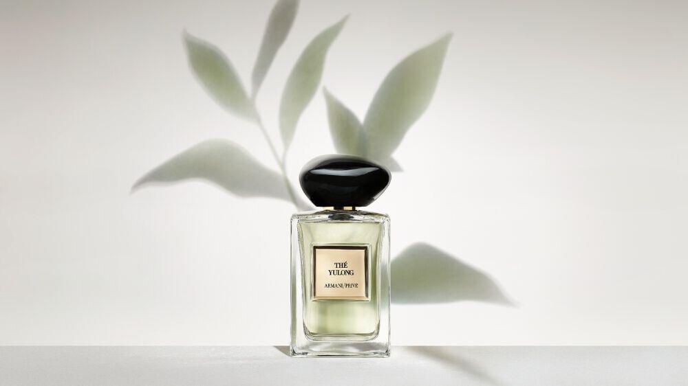 Bottle of Armani/Prive Oud Royal fragrance against a warm background with an opulent black flower.