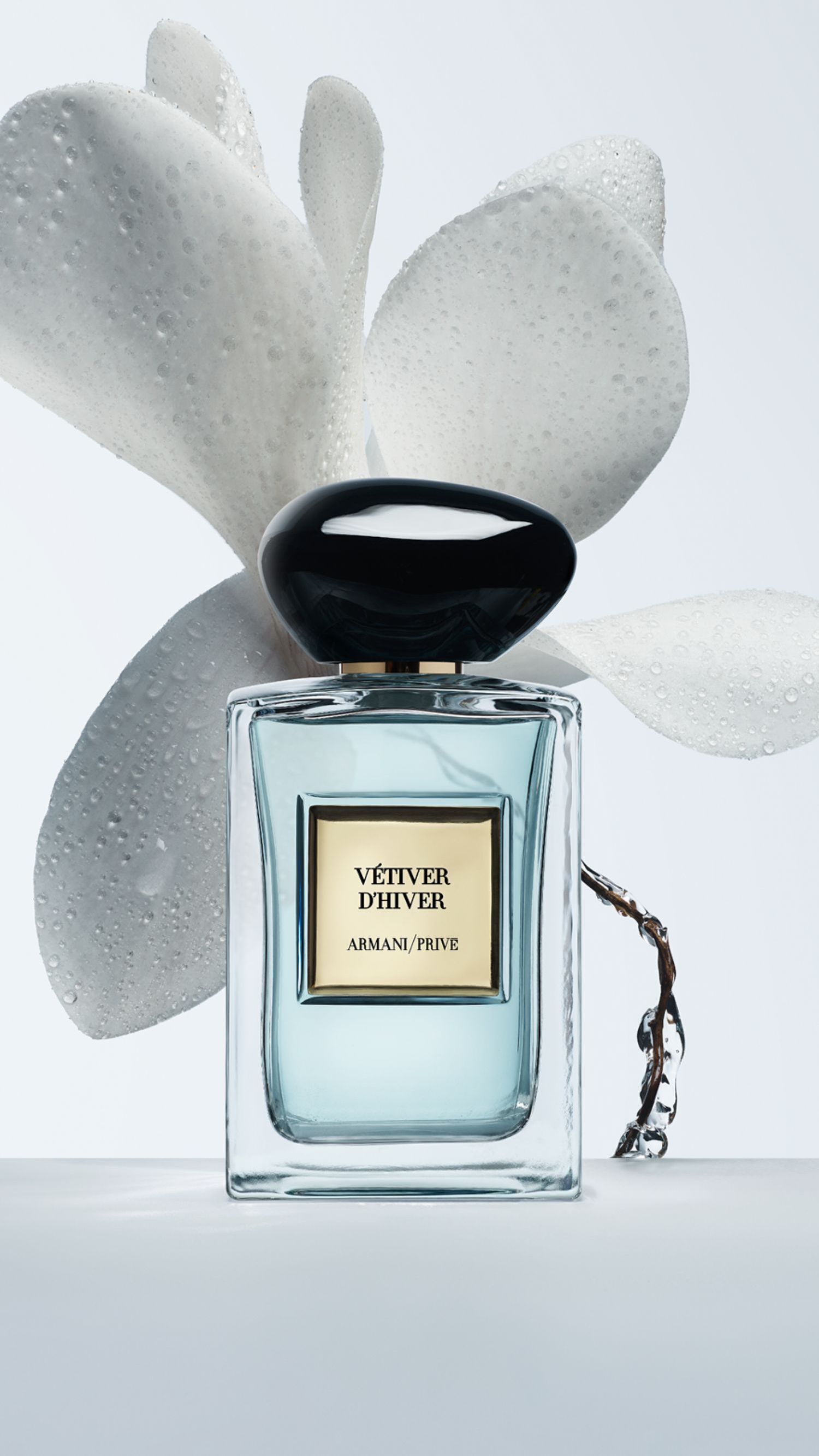 Bottle of Armani/Prive Vetiver D’Hiver against a light blue background with a white flower.