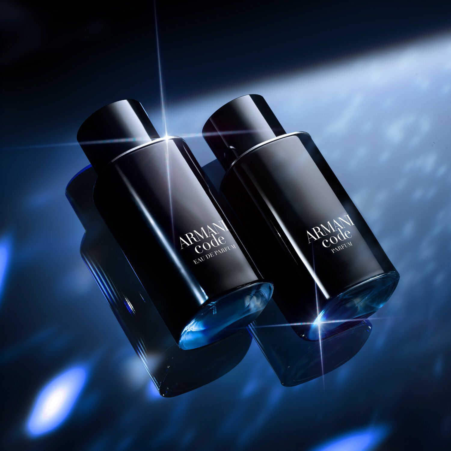 Two sleek black Armani Code bottles are displayed side by side on a reflective blue surface, illuminated by dramatic, sparkling light effects in the background.