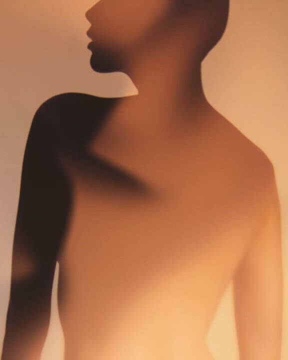 Close-up of a model's silhouette in warm, golden lighting, showcasing elegant curves and shadows for Armani Prive.