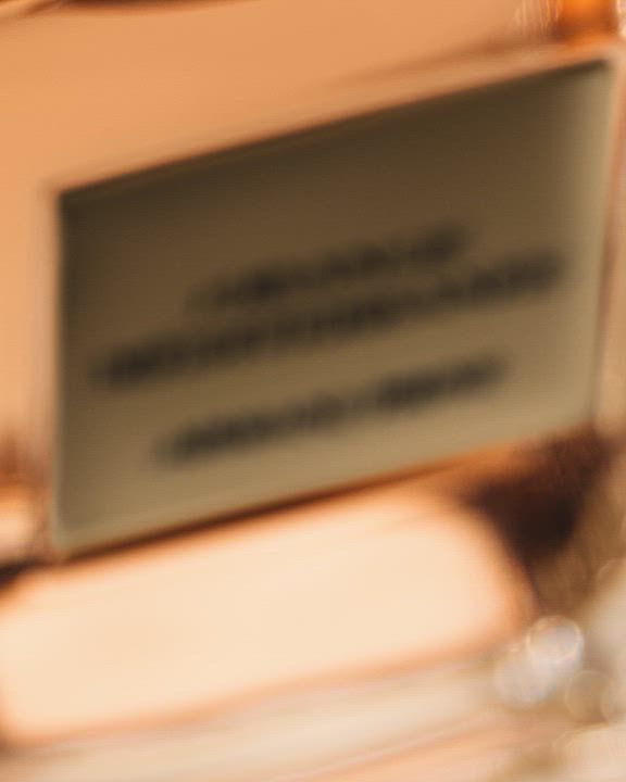 A close-up of an Armani/Prive 'Orange Mediterranee' perfume bottle with artistic overlays of a human silhouette, fresh oranges, and lemons, suggesting a vibrant and sensory experience.