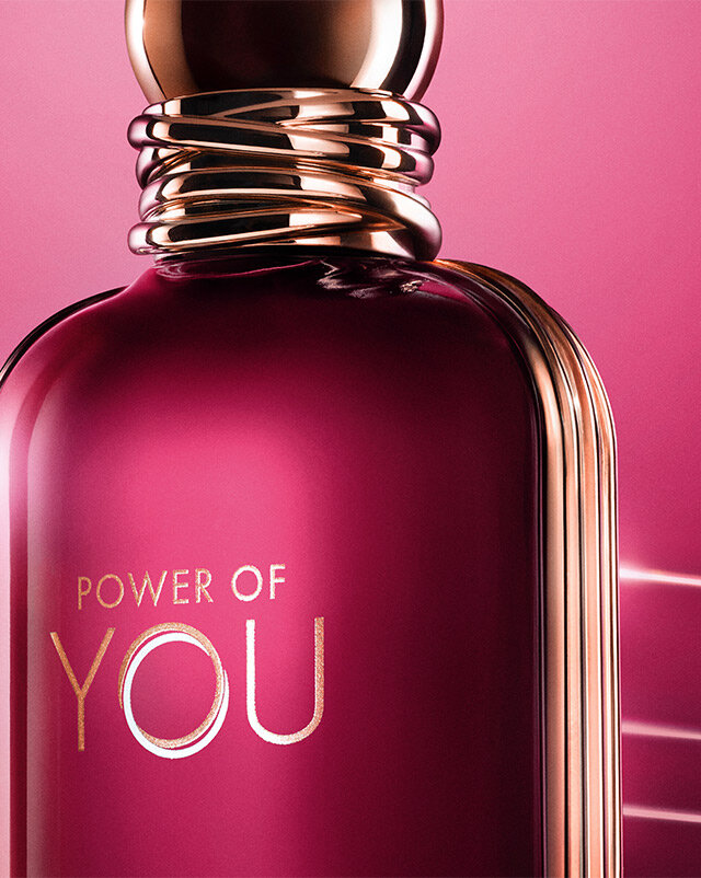 Close-up of the Armani Power of You perfume bottle, glowing in radiant ruby tones with sleek gold accents.
