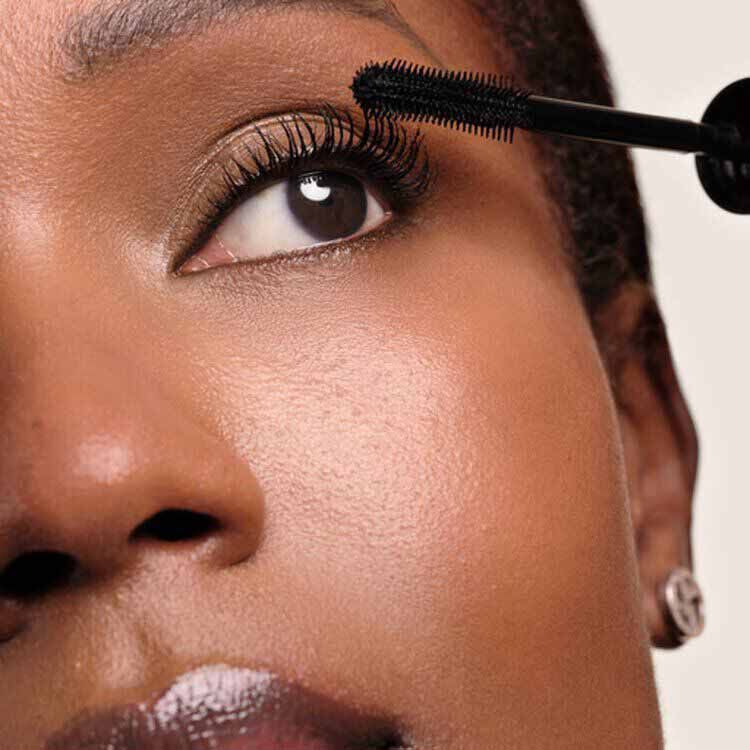 Close-up of a model applying Giorgio Armani Vertigo mascara in Obsidian Black to upper lashes with the mascara wand, showcasing defined and lengthened lash results.
