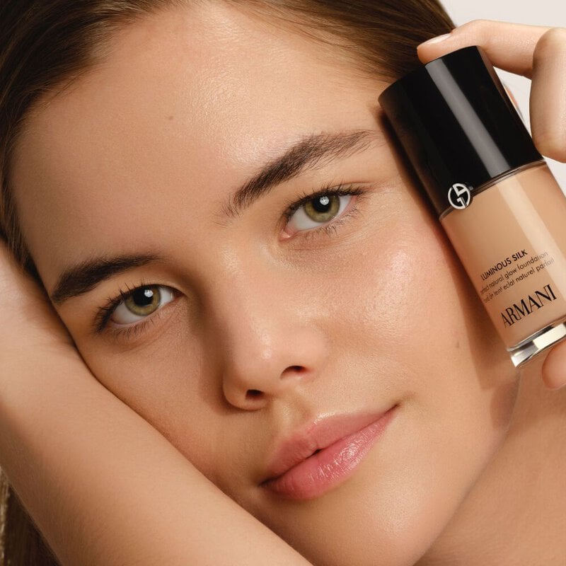 A woman holds a bottle of Giorgio Armani Luminous Silk foundation next to her face.