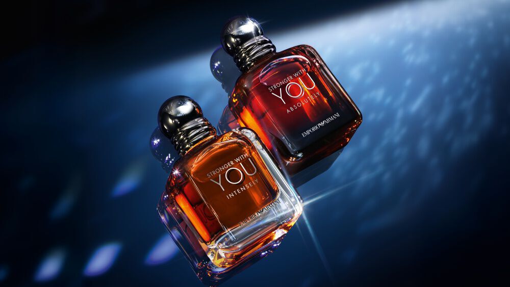  A single bottle of Emporio Armani "Stronger With You Parfum" stands upright on a reflective surface, illuminated by dramatic blue and white lighting against a dark background.