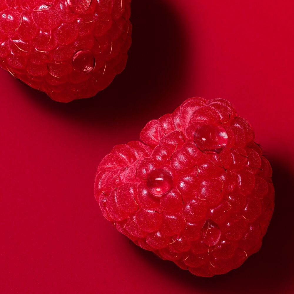 Close-up of raspberries with dewdrops on a red background.