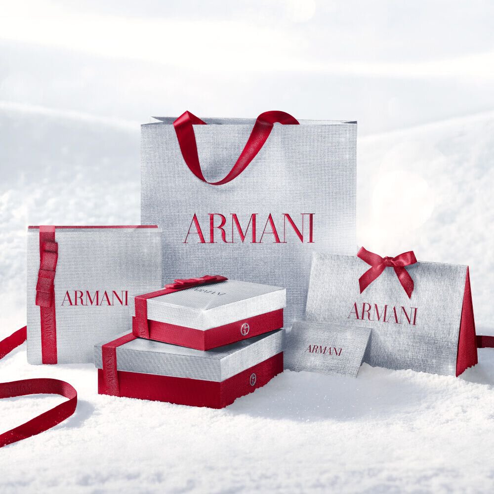 Armani beauty holiday gift bags and boxes in silver tones with red accents on snow.