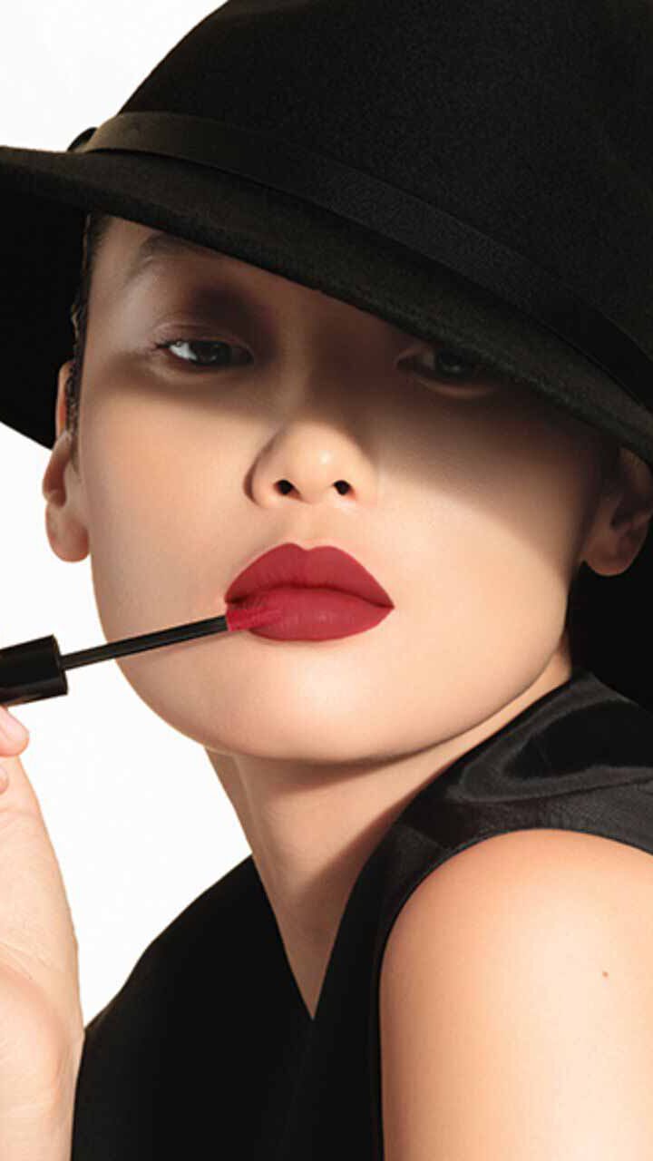 Model in a wide-brimmed black hat applying ARMANI LIP MAESTRO to her lips with the applicator.