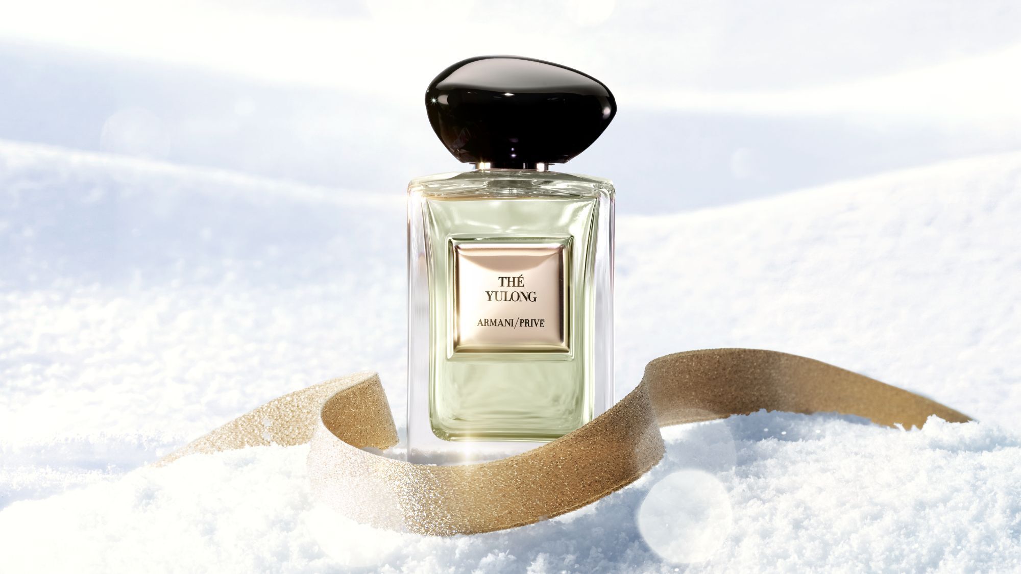 Armani Prive Les Eaux The Yulong eau de parfum, transparent rectangular glass bottle with black rounded cap, on a white snowy surface with a golden ribbon.