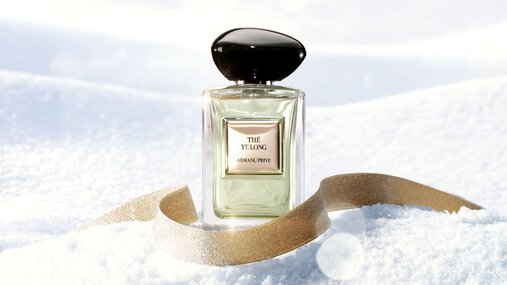 Armani Prive Les Eaux The Yulong eau de parfum, transparent rectangular glass bottle with black rounded cap, on a white snowy surface with a golden ribbon.