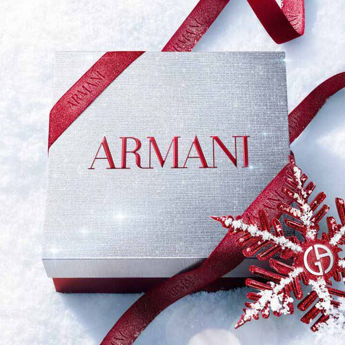 Silver Armani Glamourous Winter Holiday Gift Set box with red glitter ribbon and Giorgio Armani red snowflake ornament resting on a sparkling snowy surface — festive luxury fragrance gift packaging.