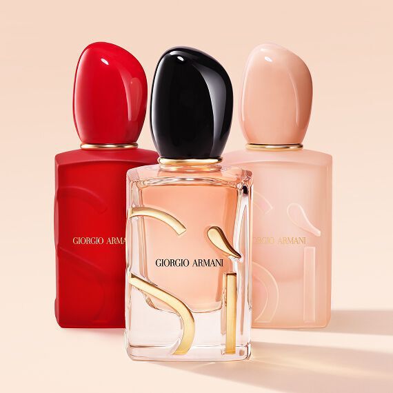 Three Giorgio Armani Si fragrance bottles in red, clear and nude pink on a nude background.